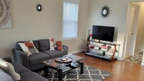 A living room with a sofa, a coffee table, a TV, and a bookshelf. - Grand View | Walk to Falls, Casino & Attractions (Niagara Falls)