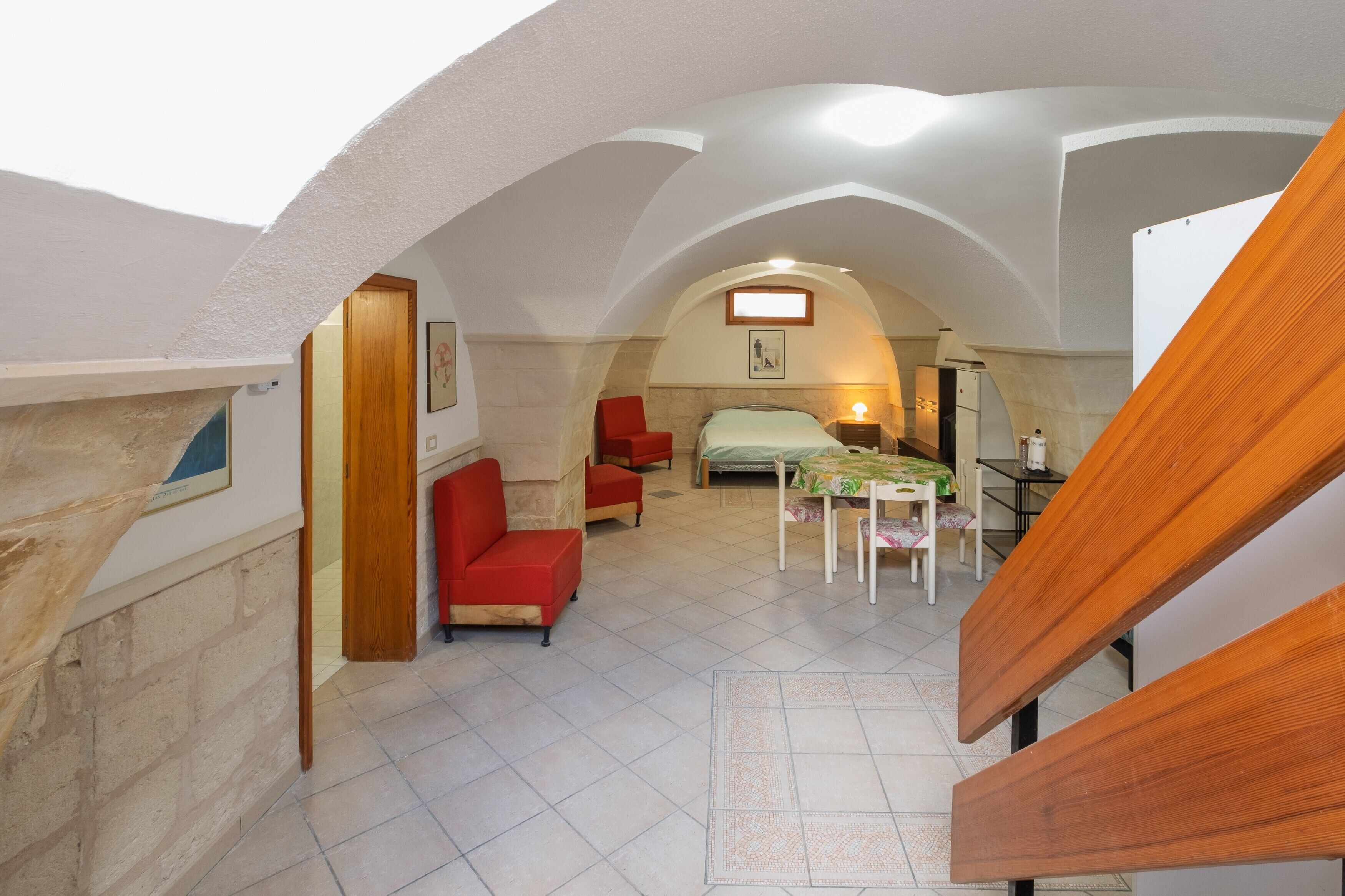 Una habitación con una cama, una mesa y sillas. Se observa una escalera de madera al frente.
