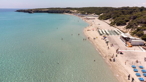 Een strand met helder water, parasols en ligbedden.