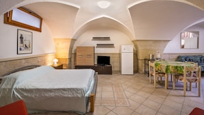 Een slaapkamer met een bed, een bureau, een stoel, een tafel met tafelkleed, een televisie, een koelkast en een raam.