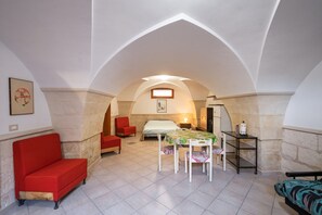 Ein gemütliches Zimmer mit einem Bett, einem roten Sofa, einem Esstisch mit Stühlen und einem kleinen Tisch mit einer Lampe.