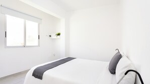 Un dormitorio minimalista con una cama grande, una ventana y un estante pequeño con una planta.