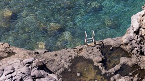 Vista despejada de una costa rocosa con una escalera metálica que desciende al agua.