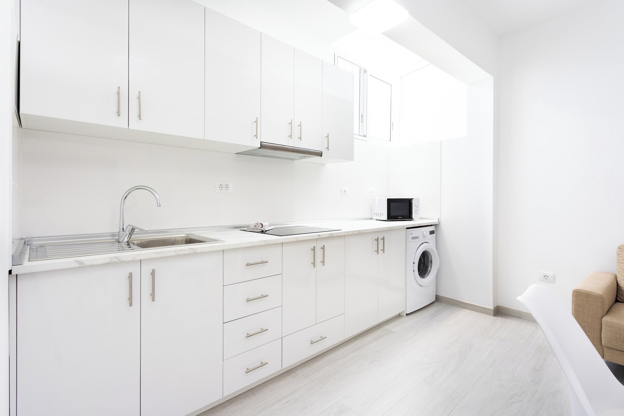 A modern kitchen with white cabinets, a stainless steel sink, and a built-in washing machine.