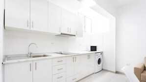 Una cocina moderna con armarios blancos, un lavamanos de acero inoxidable y una lavadora integrada.