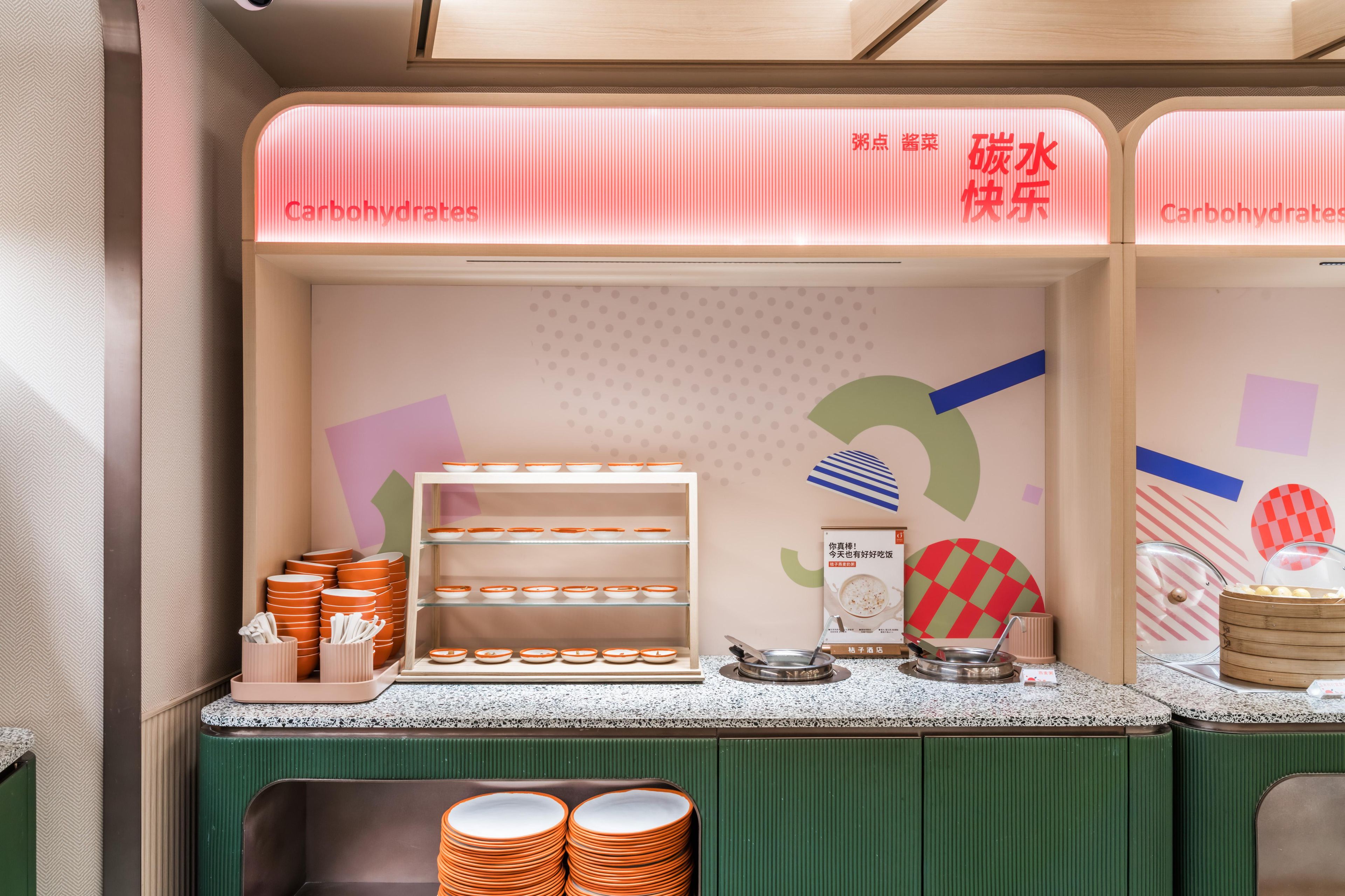 Un rincón para desayunar con una barra que muestra platos y tazones, un letrero que dice "Carbohydrates", y una pared con un diseño geométrico.
