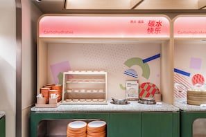 A breakfast area with a counter displaying plates and bowls, a sign reading "Carbohydrates", and a wall with a geometric pattern. - Orange Hotel Guangzhou Tianhe Sports Center (Guangzhou)