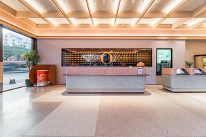 A modern reception area with a central desk, a large circular logo on the wall, and a digital display. - Orange Hotel Guangzhou Tianhe Sports Center (Guangzhou)