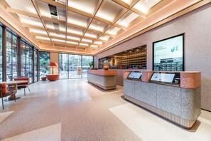 A modern reception area with a glass wall, a reception desk, and a seating area with orange chairs. - Orange Hotel Guangzhou Tianhe Sports Center (Guangzhou)