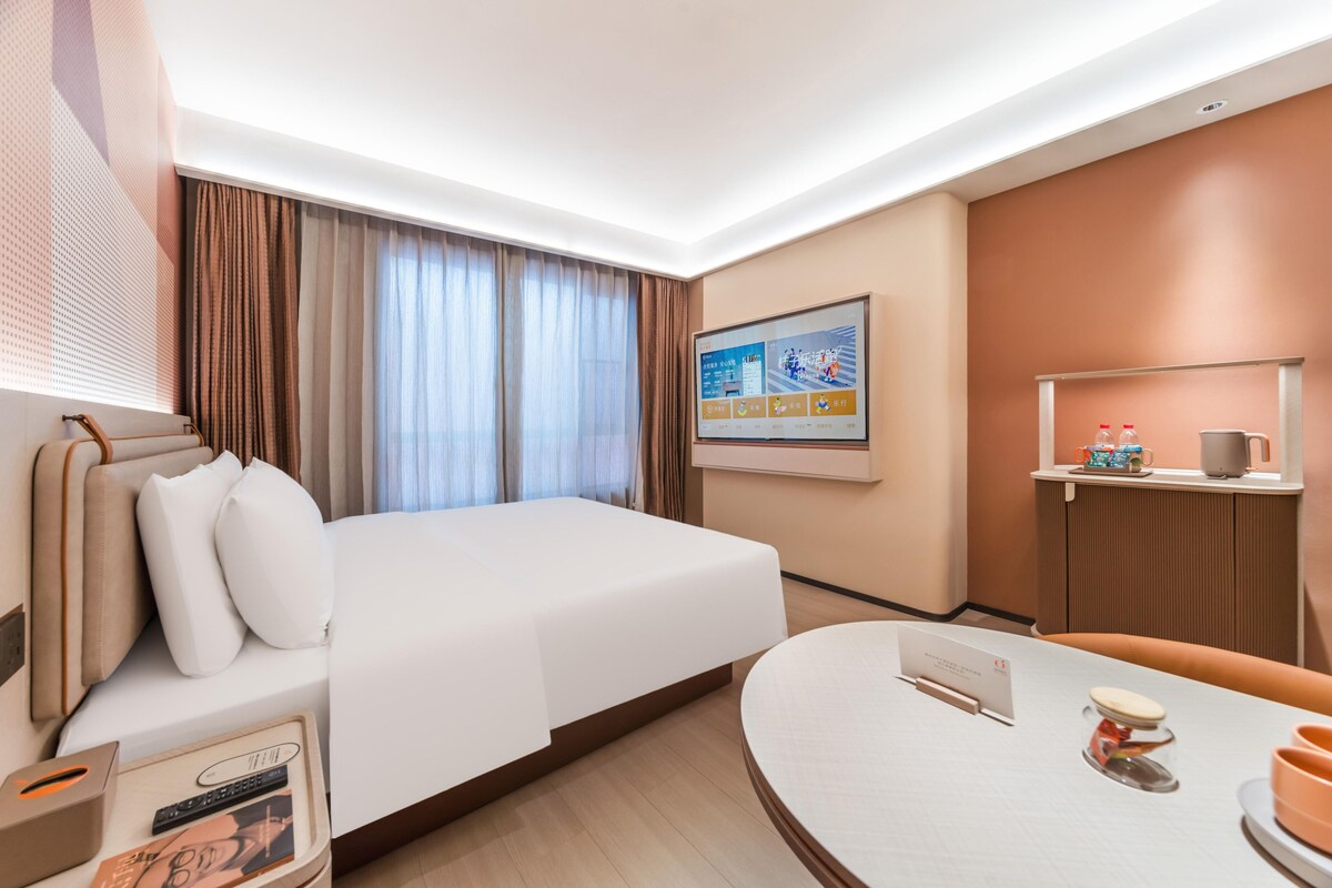 A hotel room with a bed, a desk, a chair, a TV, and a window with curtains.
