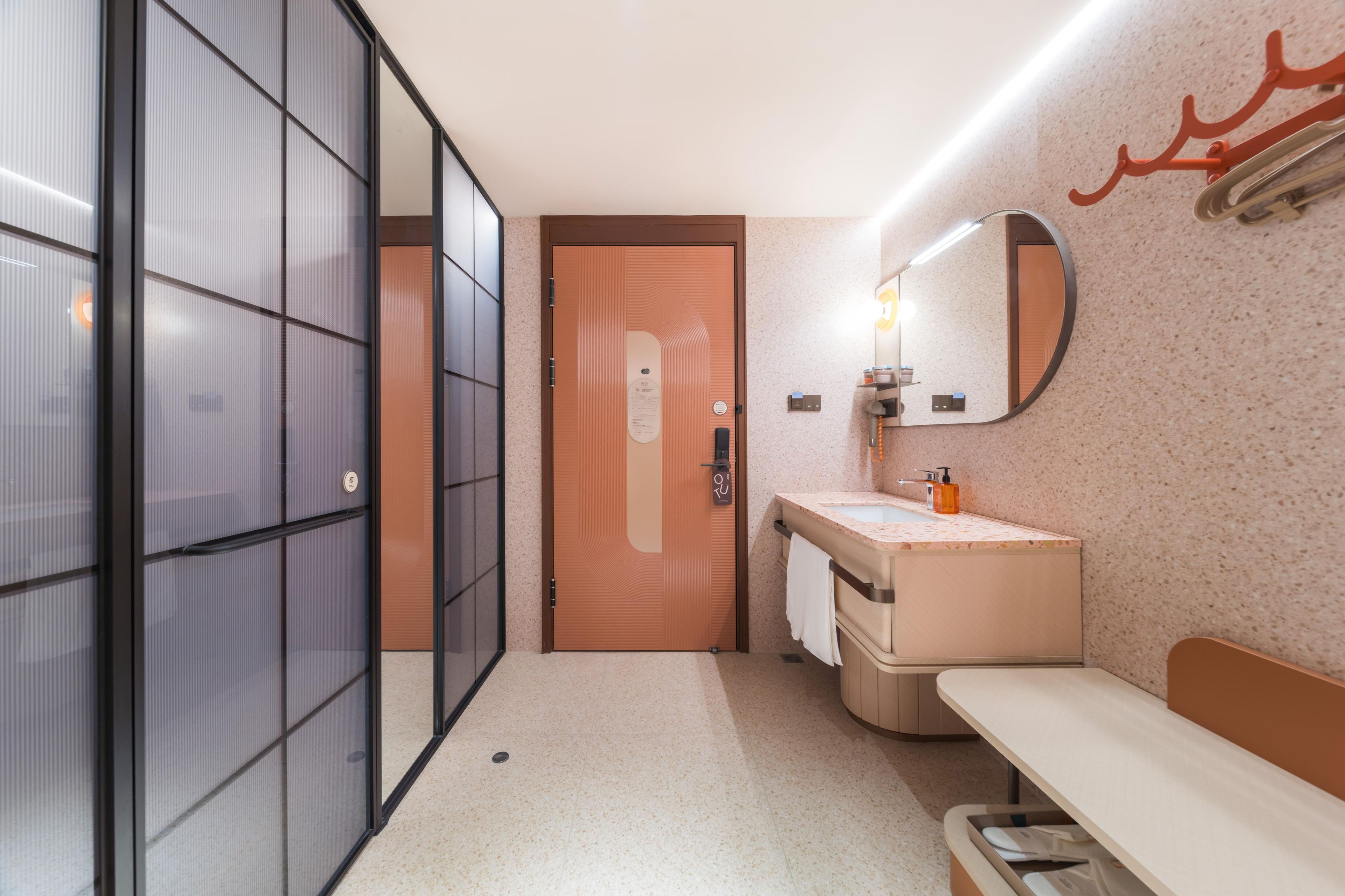 Un baño moderno con mampara de vidrio, un lavamanos con espejo y un banco.