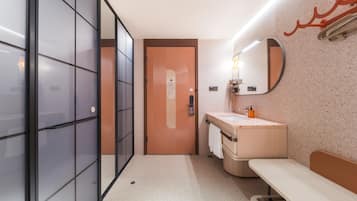 Un baño moderno con mampara de vidrio, un lavamanos con espejo y un banco.