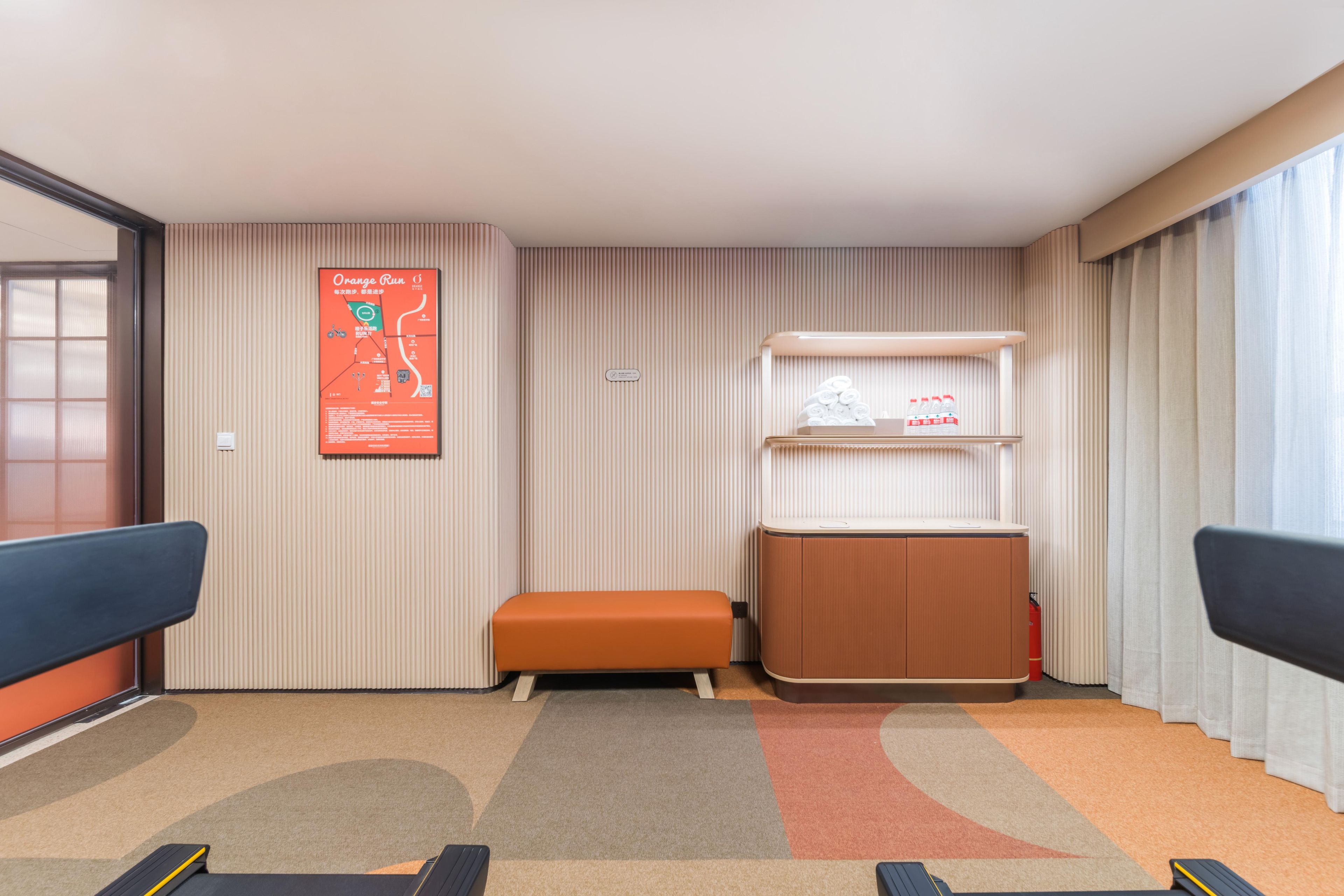 A hotel room with a large window, a poster on the wall, a bench, a small table, and a carpeted floor.