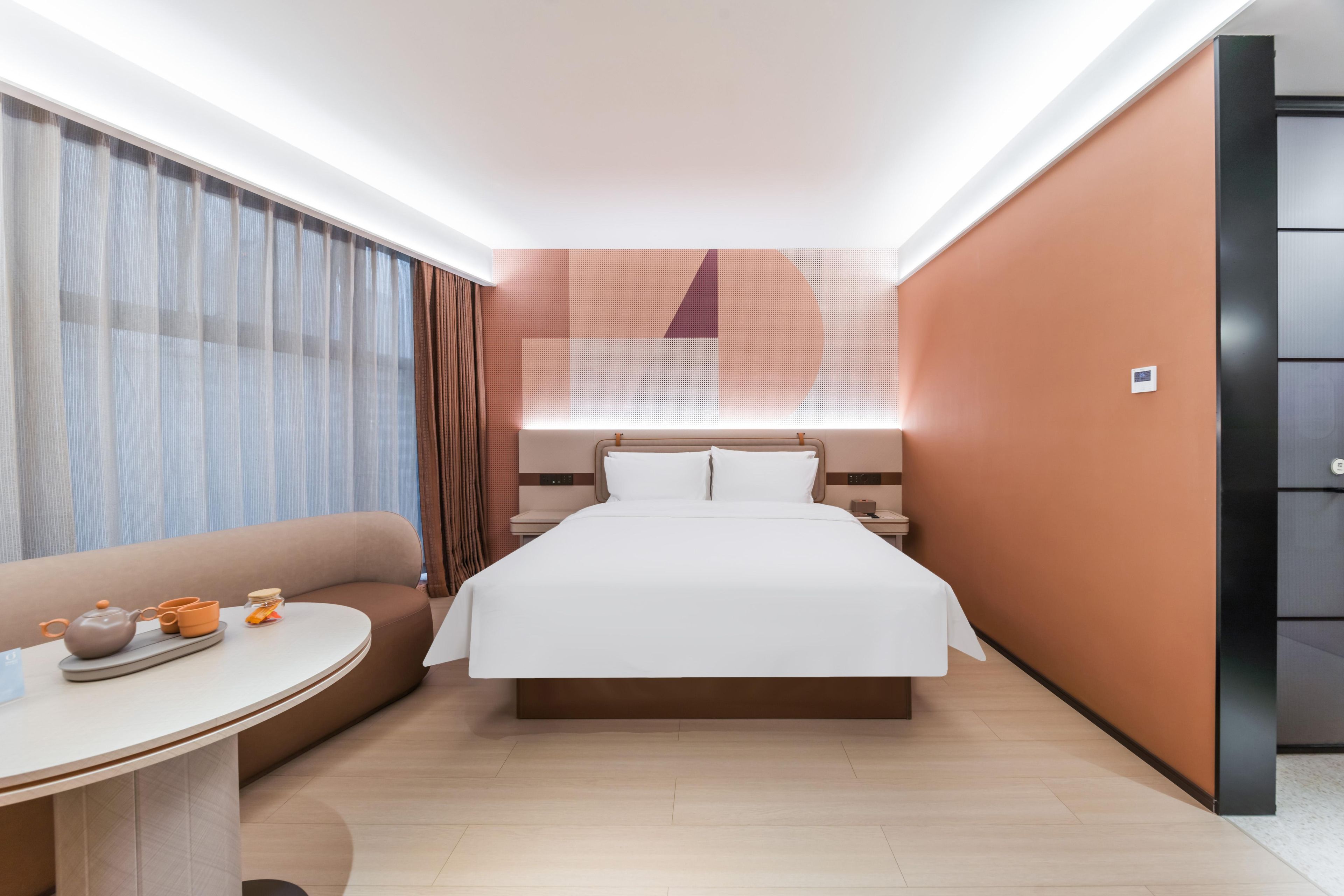 A modern hotel room with a large bed, a sofa, a small round table with tea set, and a wall-mounted TV.