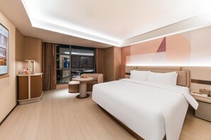 A modern hotel room with a large bed, a small round table, a sofa, and a desk with a lamp. - Orange Hotel Guangzhou Tianhe Sports Center (Guangzhou)