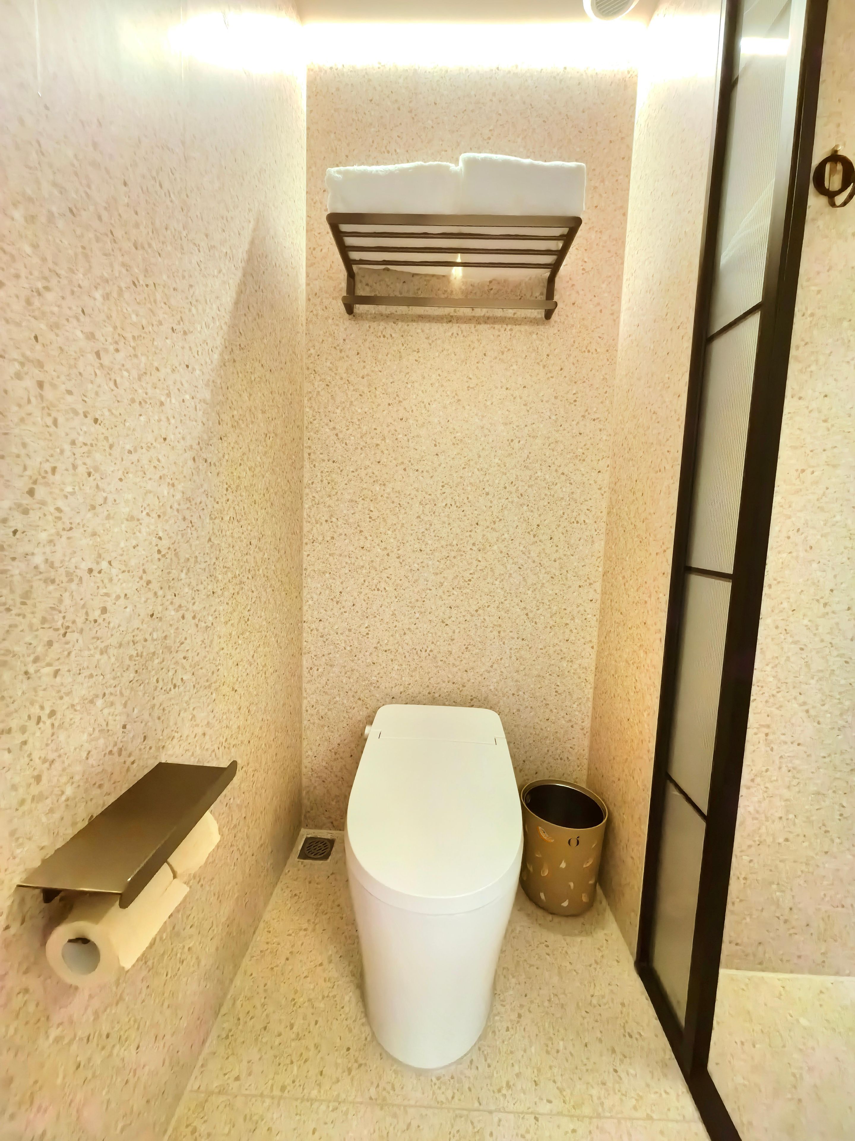 Casa de banho pequena e compacta, com sanita, um cesto de lixo e suporte para papel higiénico.
