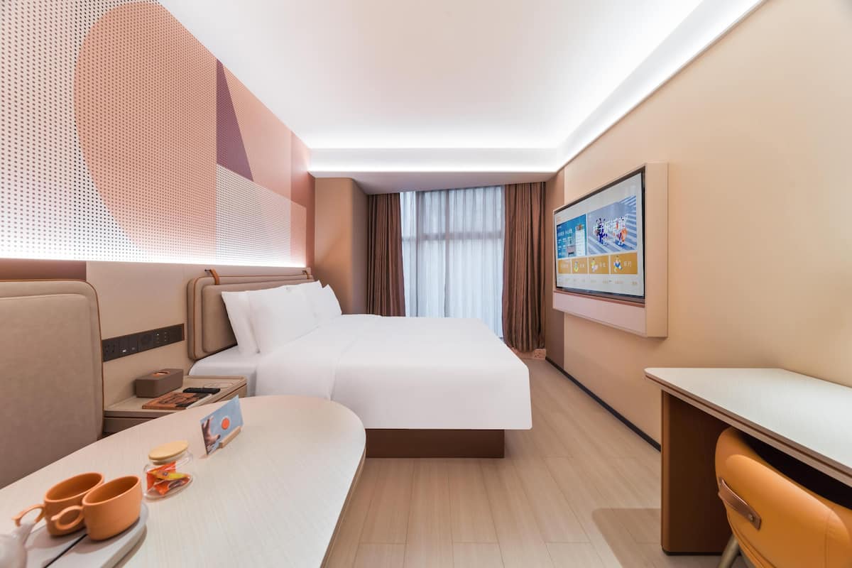 A modern hotel room with a large bed, a desk, and a seating area.