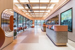 A modern hotel lobby with a reception desk, seating area, and large windows offering views of the outdoors. - Orange Hotel Guangzhou Tianhe Sports Center (Guangzhou)