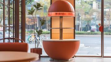 Interior moderno com uma luminária laranja grande, plantas em vasos e vista da rua através de grandes janelas.