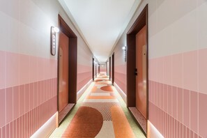 A long, narrow hallway with a patterned carpet, wooden doors, and a light fixture on the wall. - Orange Hotel Guangzhou Tianhe Sports Center (Guangzhou)