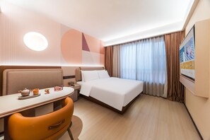 A hotel room with a bed, a desk with a chair, a table with a teapot and cups, and a wall-mounted TV.