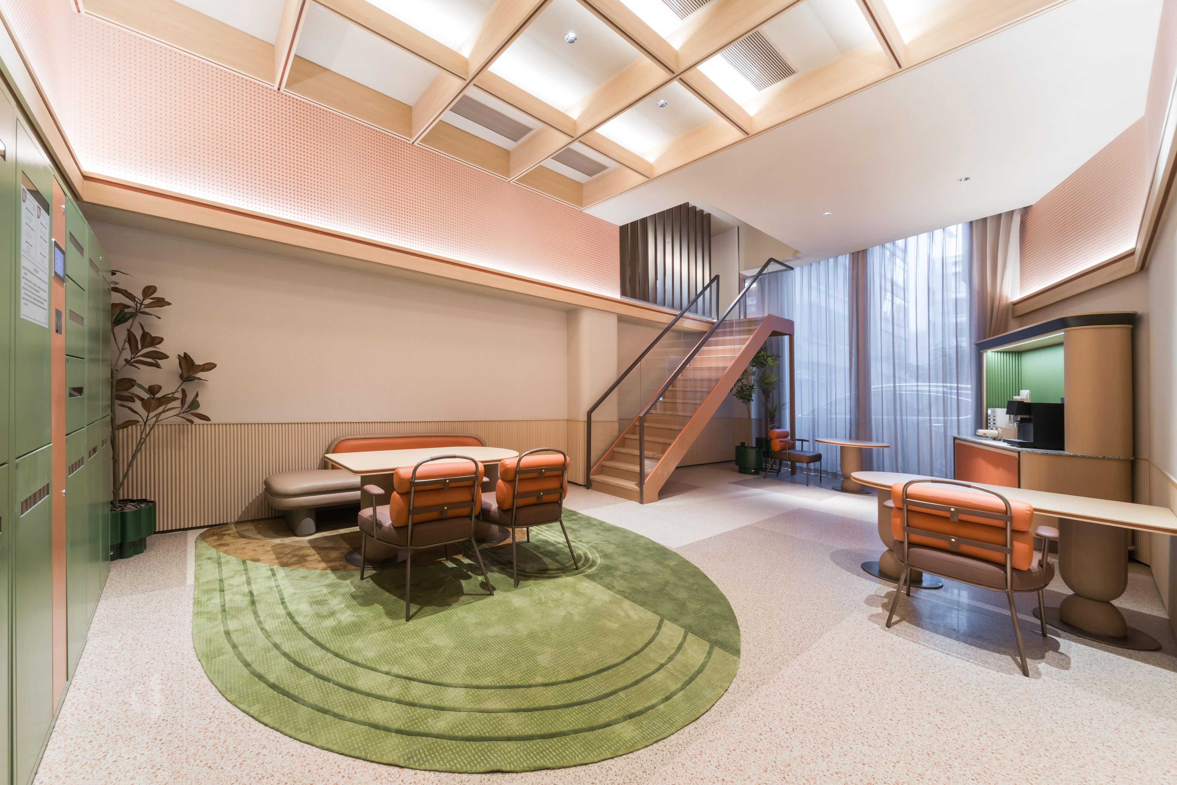 A modern interior with a staircase, a dining area with a green rug, and a seating area with orange chairs.
