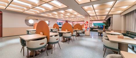 Un comedor moderno con mesas y cabinas, techo con diseño y una ventana circular.