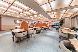 A modern dining area with tables and booths, a patterned ceiling, and a circular window. - Orange Hotel Guangzhou Tianhe Sports Center (Guangzhou)