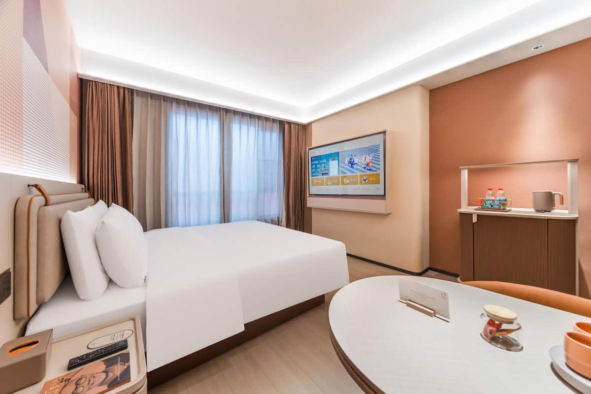 A hotel room with a bed, a desk, a chair, a TV, and a window with curtains.