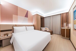 Ein Hotelzimmer mit einem großen Bett, einem Schreibtisch mit Telefon, einem Sessel, einem kleinen Tisch mit Tasse und einem Schrank.