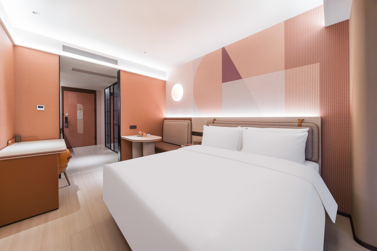 A modern hotel room with a large bed, a desk, and a small table.