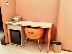 A compact hotel room with a small desk, a compact refrigerator, a trash bin, and a chair with a leather seat. - Orange Hotel Guangzhou Tianhe Sports Center (Guangzhou)