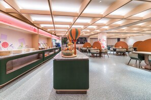A modern dining area with a central island, seating arrangements, and a counter with food items. - Orange Hotel Guangzhou Tianhe Sports Center (Guangzhou)