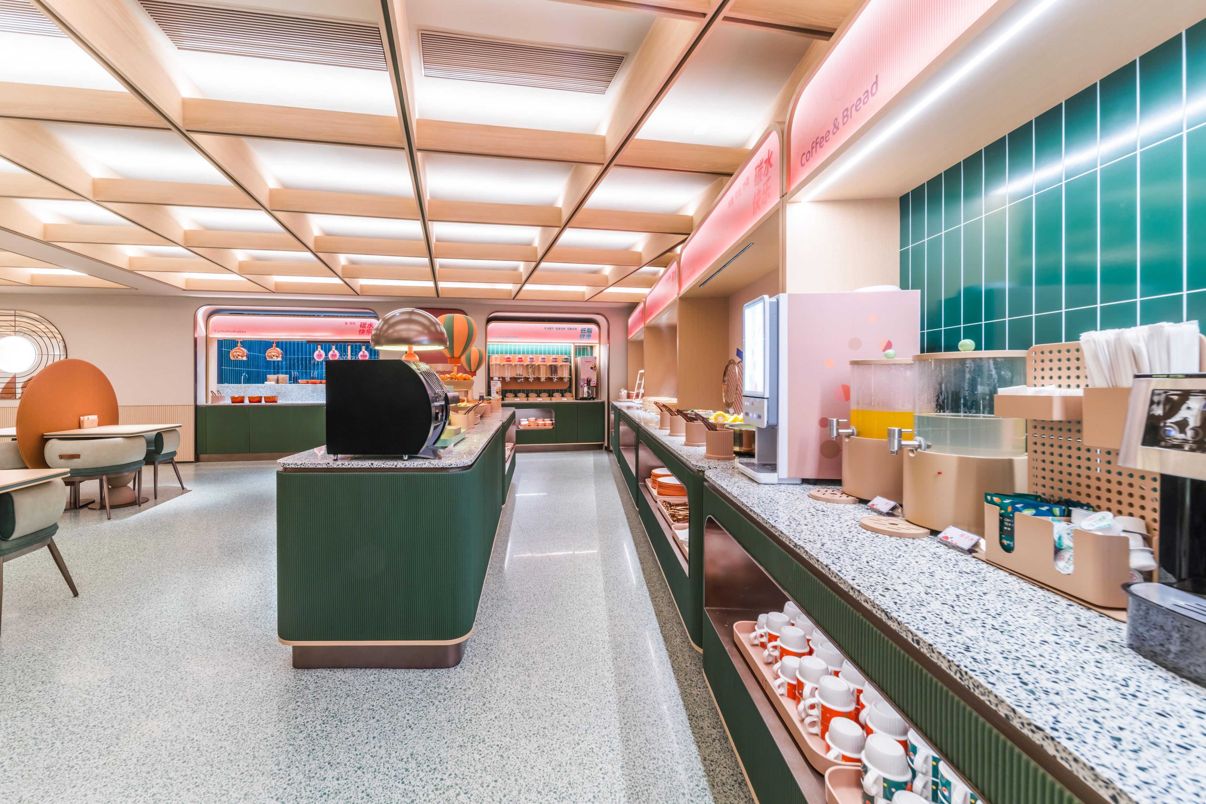 Interior de una cafetería moderna con mostrador central, zona de estar y exhibición de alimentos.