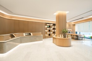 A modern reception area with a curved reception desk, a central pillar with a plant, and a seating area with tables and chairs. - Ji Hotel Guangzhou Sanyuanli Medicine University (Guangzhou)