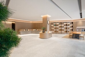 Un'area reception moderna con una scrivania centrale, un angolo relax con un tavolo e una libreria piena di libri.