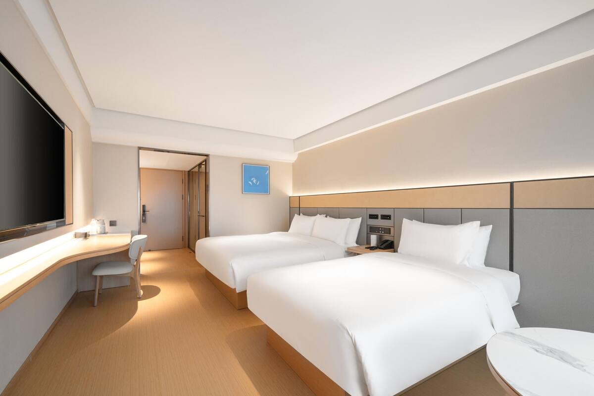 Ein modernes Hotelzimmer mit zwei Betten, einem Schreibtisch und einem Fernseher.