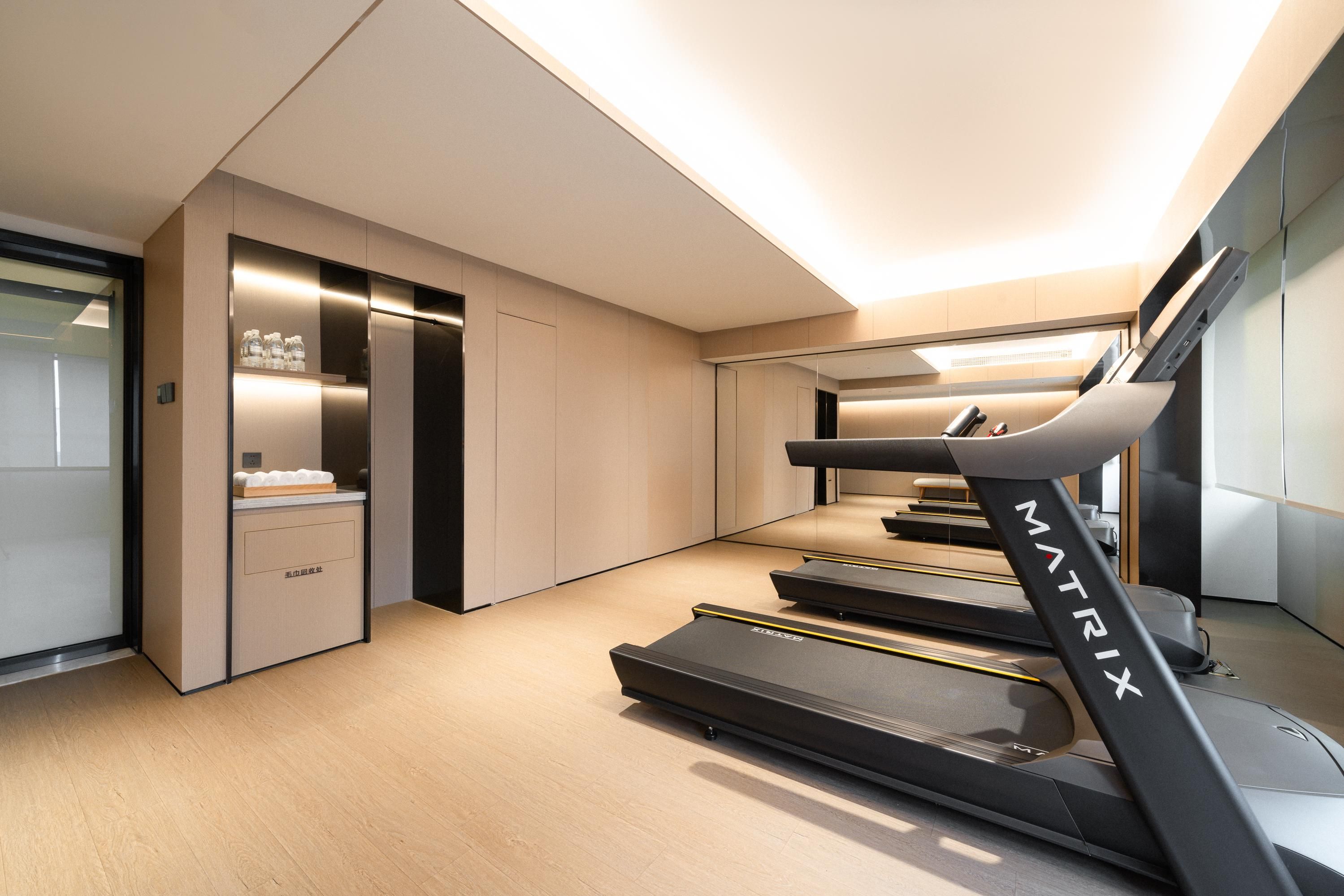 A modern hotel room with a treadmill, a minibar, and a mirror.