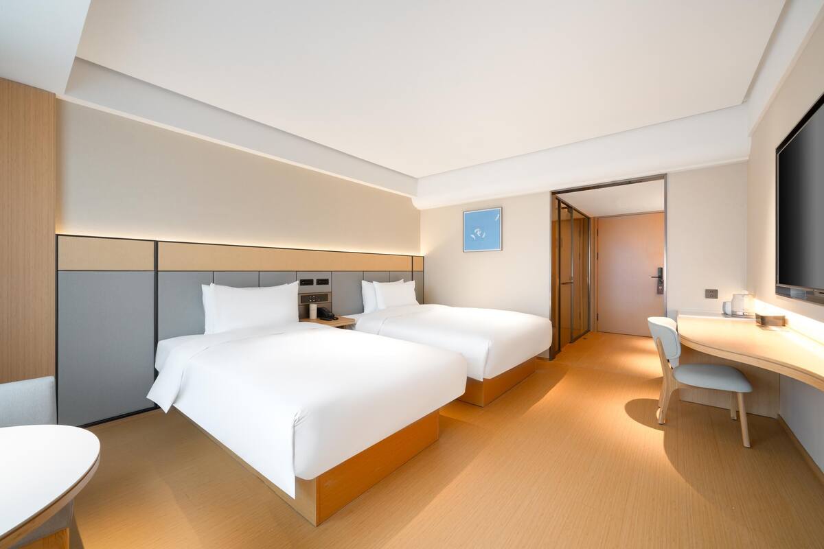 Ein modernes Hotelzimmer mit zwei Betten, einem Schreibtisch und einem Sessel.