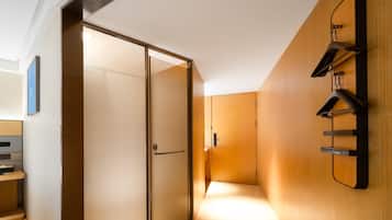 Quarto de hotel moderno com porta de vidro deslizante, porta-roupas de madeira fixado na parede e design minimalista.