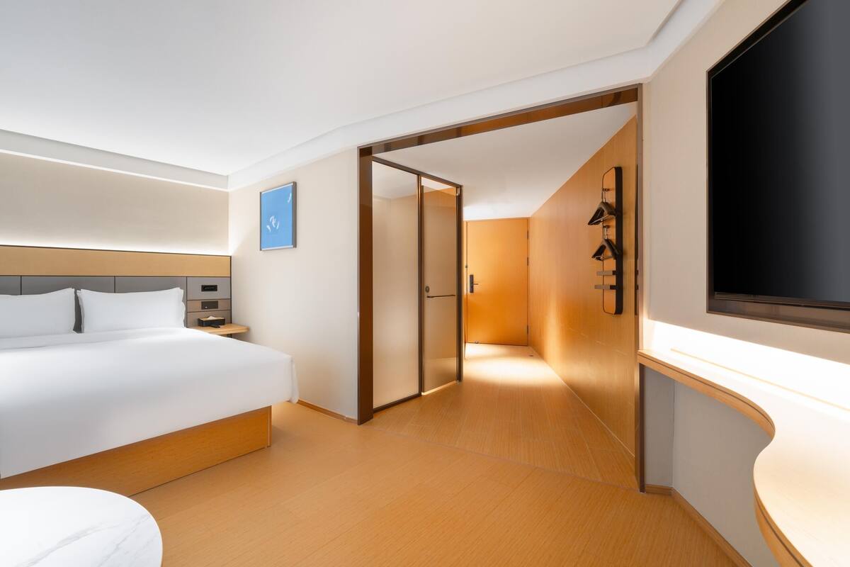 Ein modernes Hotelzimmer mit einem großen Bett, einem Fernseher, einem Schreibtisch und einem begehbaren Kleiderschrank.