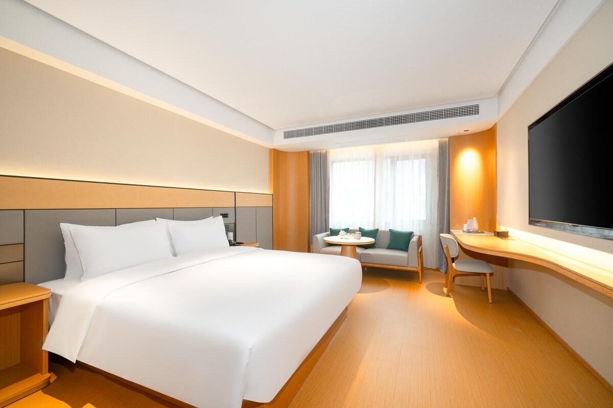 A hotel room with a large bed, a desk, a chair, a small table, and a TV.