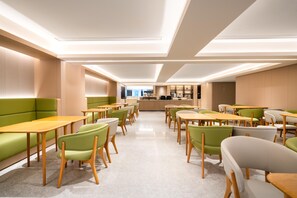 A modern dining area with green booths and wooden tables, featuring a central counter and a view of the city. - Ji Hotel Guangzhou Sanyuanli Medicine University (Guangzhou)