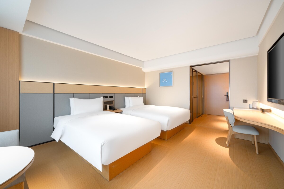 A modern hotel room with two beds, a desk, and a chair.