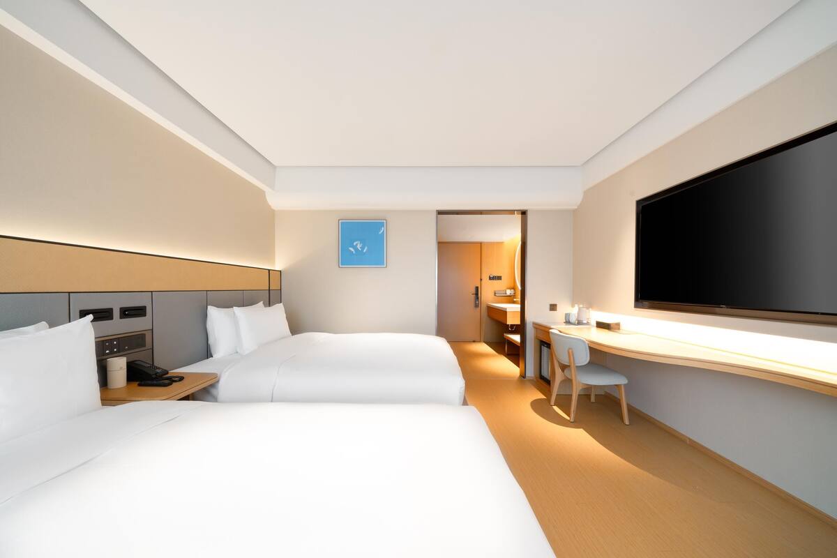 Ein Hotelzimmer mit zwei Betten, einem Schreibtisch, einem Fernseher und einem durch eine offene Tür einsehbaren Badezimmer.