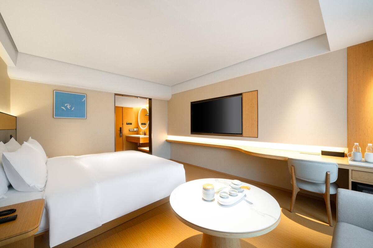Ein Hotelzimmer mit Bett, Schreibtisch, Stuhl, Fernseher und einem kleinen Tisch mit Tassen und einer Flasche.