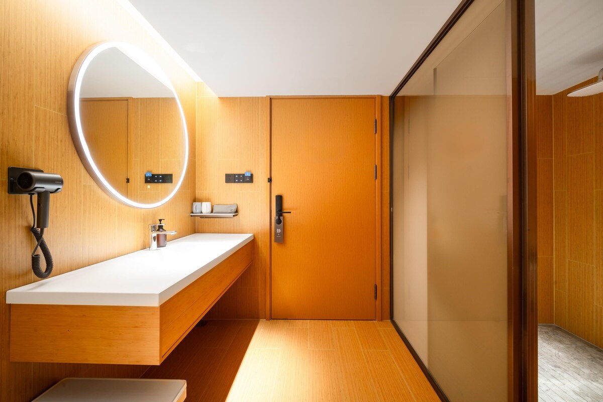 A modern bathroom with a wooden vanity, a large mirror with built-in lighting, a hairdryer, and a towel rack.