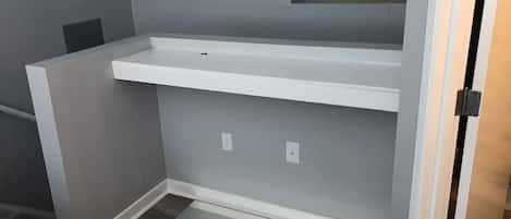 Una habitación con una estantería blanca empotrada en una pared gris, una puerta con pomo negro y suelo de madera.