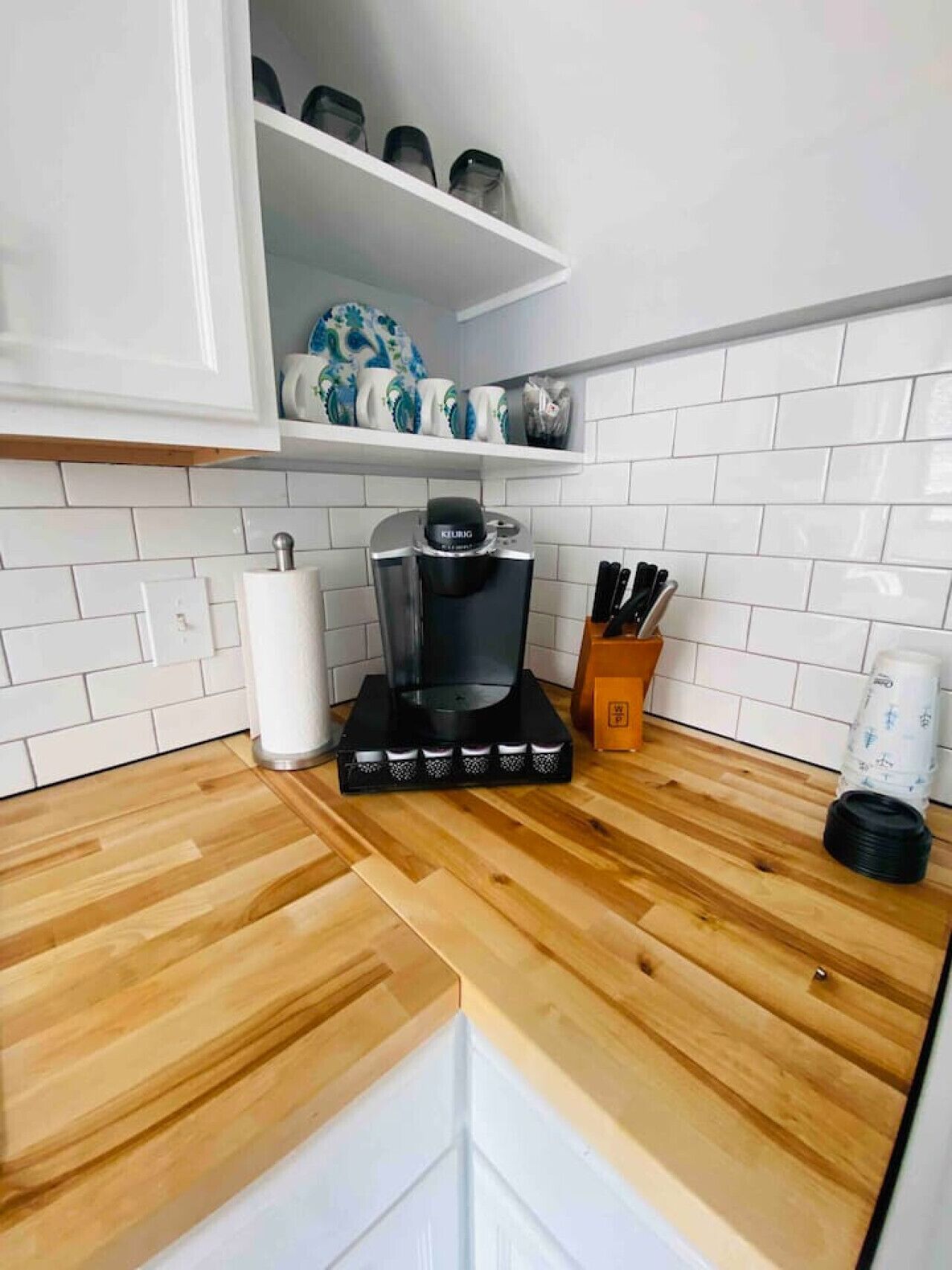 Cozinha com armários brancos, uma cafeteira, um bloco de facas e uma prateleira com objetos decorativos.