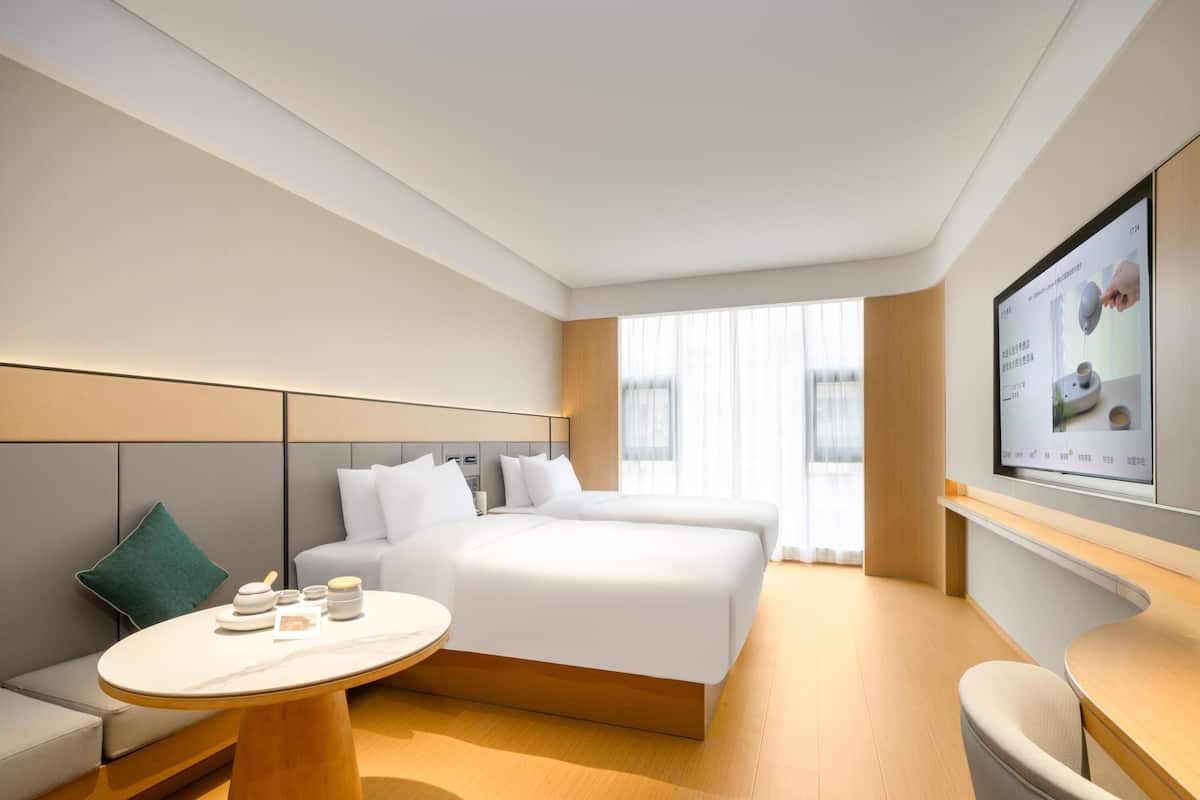 A modern hotel room with a large bed, a small round table, a sofa, and a TV mounted on the wall.